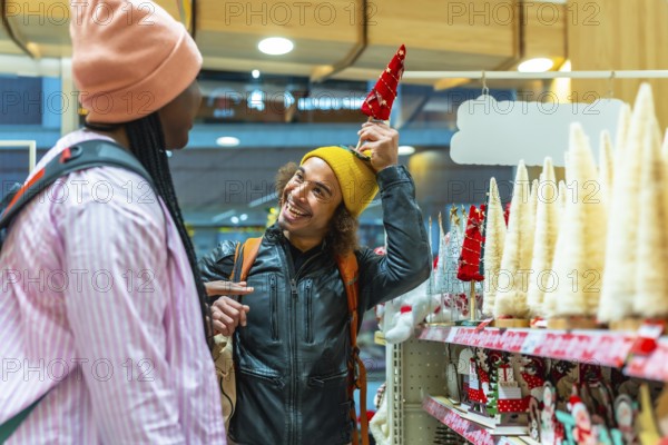 Diverse young couple laughing and shopping for festive holiday decorations in a bright store,