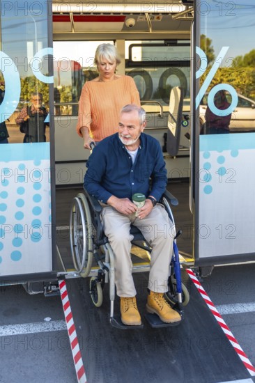 Senior woman is confidently assisting a mature man in a wheelchair to exit a public bus using the