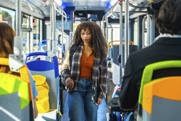 Young woman passenger with long curly hair and glasses walking along the aisle of a public bus,