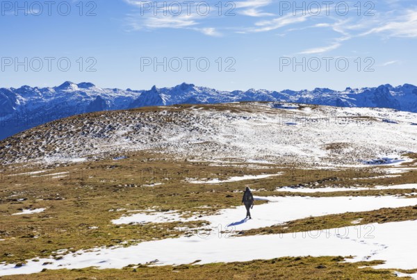 Female hiker walks across a snowfield on the Trattberg Alm with a view of the Tennengebirge,