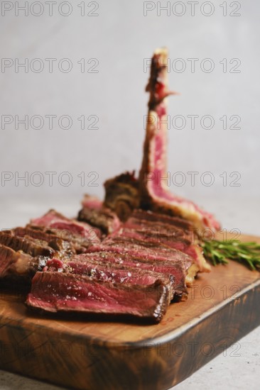 Thick slices of perfectly cooked t-bone steak medium rare on a wooden cutting board. Fresh herbs
