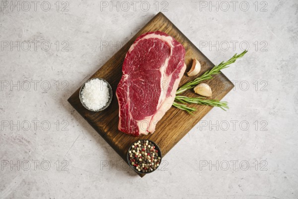 Raw ribeye roll steak rests on a wooden cutting board alongside garlic cloves and fresh rosemary.