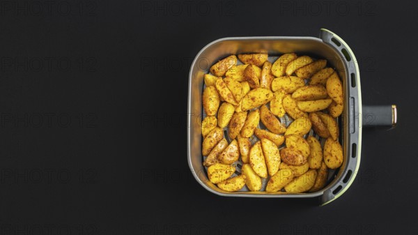 Top view of golden brown potato wedges in an air fryer basket against a dark background. These