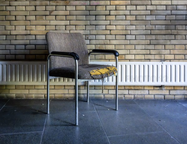 Retired and broken old office chair stands in front of a small radiator in an office building,