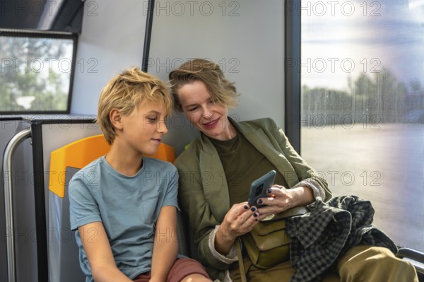 Mother and son sharing a smile as they browse a smartphone together on a city bus, enjoying a