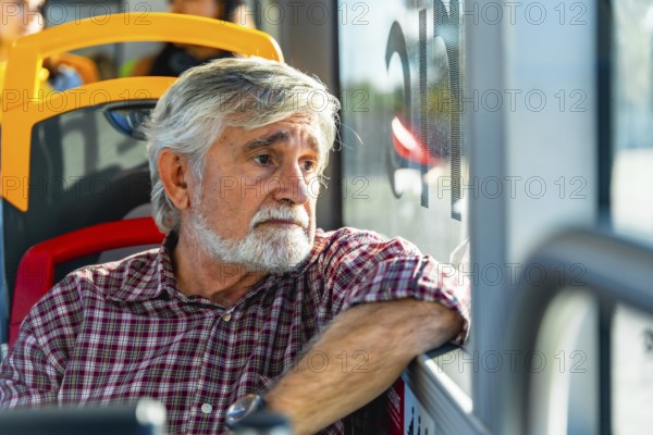 Senior man with gray hair and beard traveling on a public bus, wearing a plaid shirt and looking