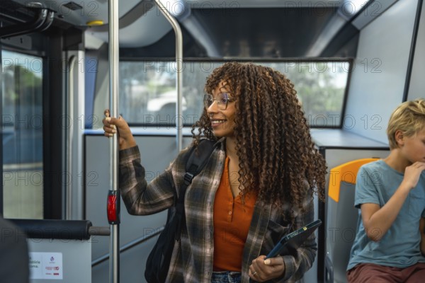 Woman with glasses and curly hair holding a digital tablet while commuting on a public bus, smiling