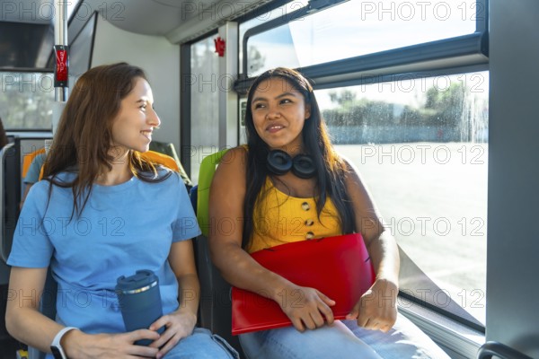 Two young diverse women students chatting and smiling on a city bus, enjoying a relaxed commute