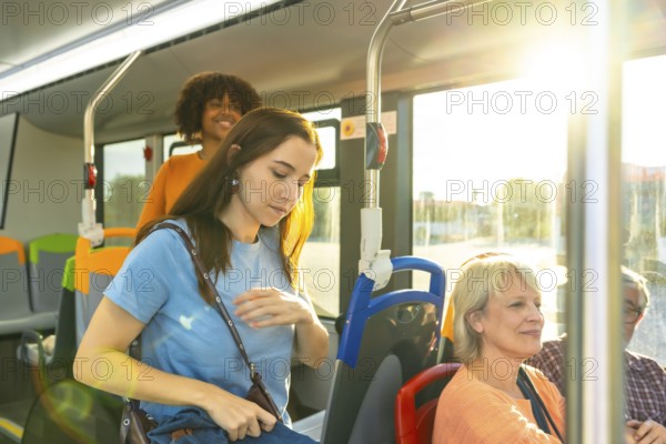 Diverse commuters on a city bus in sunlight, young woman looking down while other passengers sit