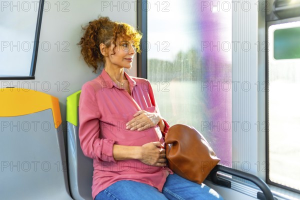 Pregnant woman sitting on a public bus, holding her belly, and looking out the window while