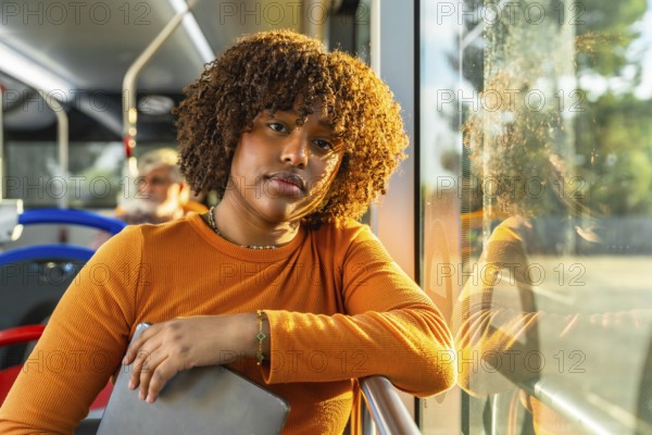 Young black woman with curly hair traveling on public transport, catching golden hour daylight