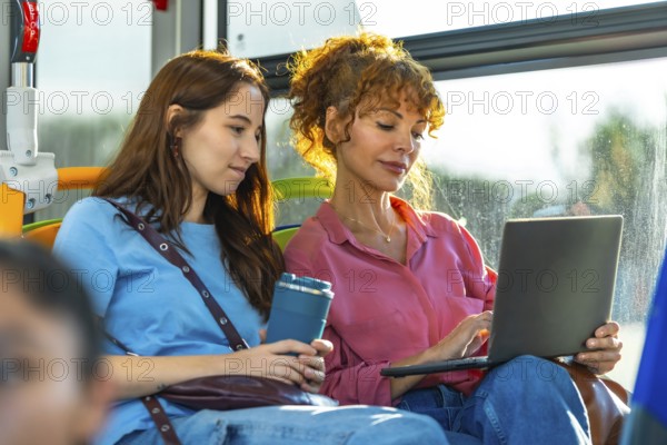 Two women traveling on public transport, one working on a laptop, demonstrating remote work