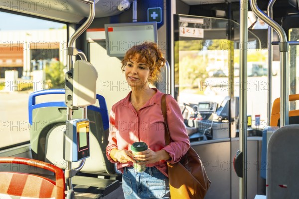 Woman standing on a city bus during the morning commute, holding a reusable coffee cup and brown