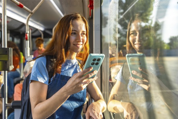 Young woman smiling on a sunny bus commute, holding her smartphone and looking out the window with