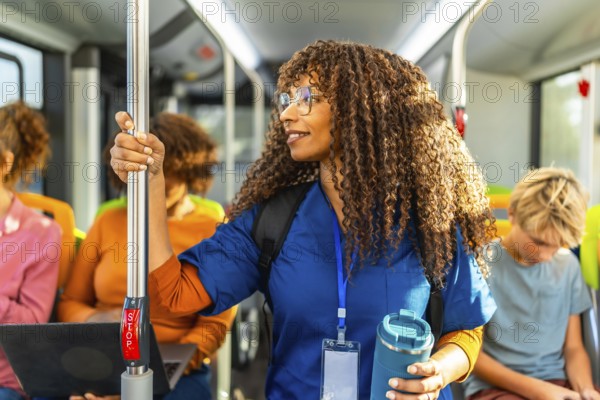 Healthcare professional with curly hair standing in a public transport bus, wearing scrubs while