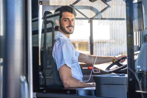 Young man working as a bus driver, smiling at the viewer while steering the public transport