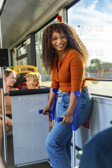 Smiling young woman with crutches standing in a public city bus, commuting happily while other