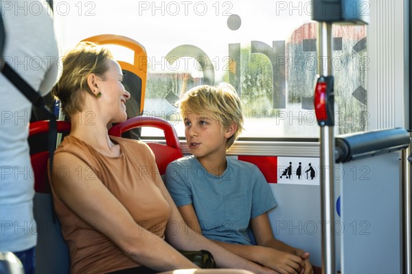 Mother and son smiling and chatting on a sunlit city bus during their commute, sharing a relaxed