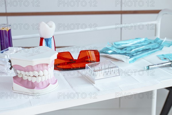 Various instruments, dental models, and hygiene items are laid out on the table in the dental