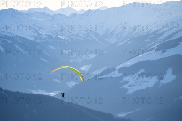 Paragliders flying over snowy mountain peaks in winter in evening light, Kitzbühel Alps, Tyrol,