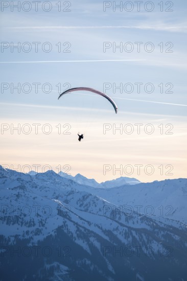 Paragliders flying over snowy mountain peaks in winter in evening light, Kitzbühel Alps, Tyrol,