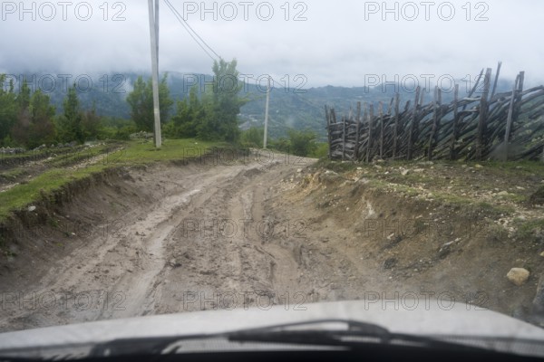 Muddy dirt road in a rural area leads through nature, four-wheel drive Lada, Imereti region,