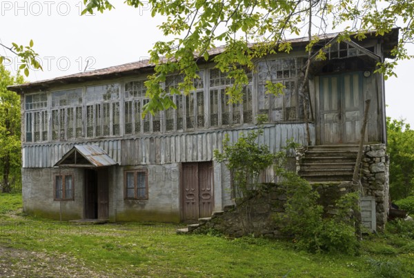 Old wooden house with lots of windows surrounded by trees in the countryside, Imereti region,