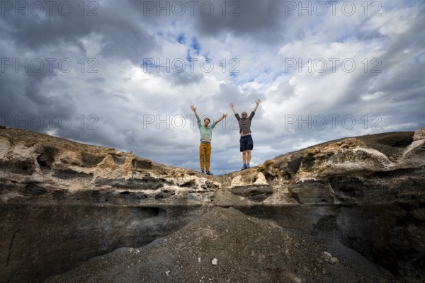 Two young men stretch their arms in the air, Eroded rock formations in volcanic landscape with