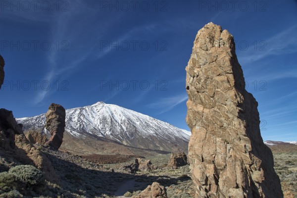 Snow-capped Teide, towering rock formations in front of a snow-capped mountain under clear skies,