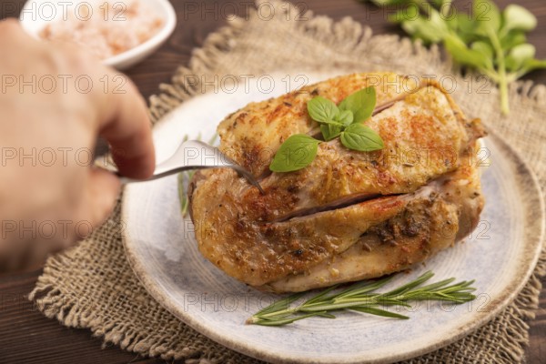 Fried Turkey Thigh with spices and rosemary on plate with hand on brown wooden background and linen