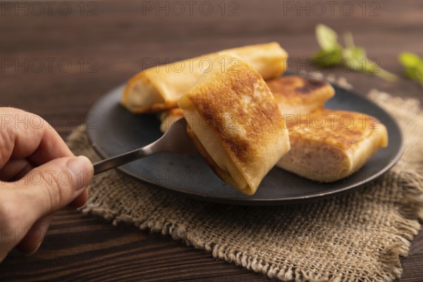 Fried crispy pancakes with meat and cheese with hand on brown wooden background and linen textile.