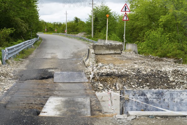 Partially closed road with signs and debris surrounded by green vegetation, bridge over the Techuri