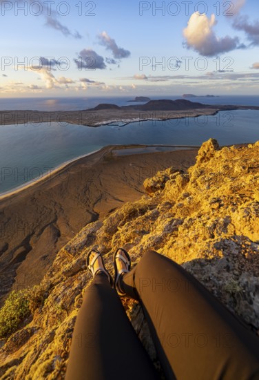 First person view, legs of a woman sitting on a steep cliff, view of the sea and the island of La