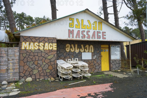 Colourful building with massage signs and stacked loungers outside, beach massage equipment with