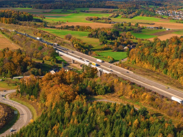 Road with bridge through autumn landscape with green fields and wooded hills, A8 near Rutesheim,