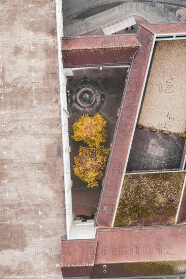 Aerial view of a courtyard with a fountain and yellow trees, surrounded by a large building with a