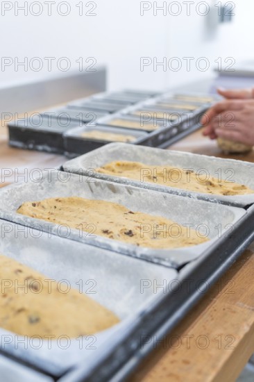 Dough in loaf pans, hands of a baker working dough in the background, Christmas baking,