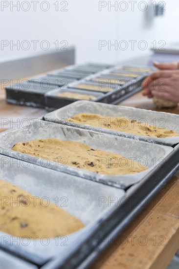 Close-up of dough in loaf pans, hands of a baker visible in the background, Christmas baking,