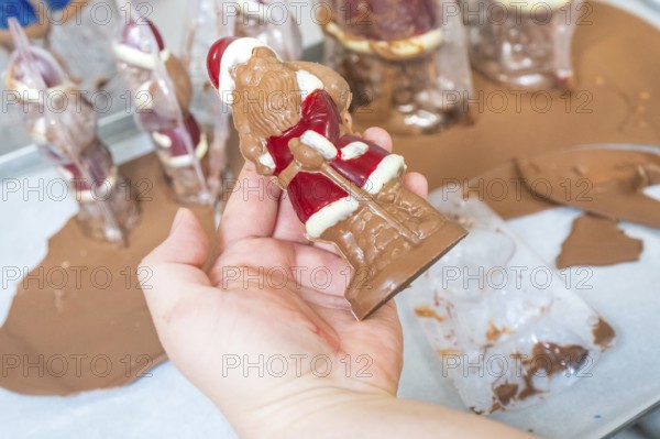 One hand holds a half-finished chocolate Santa Claus on a work surface, Christmas baking,