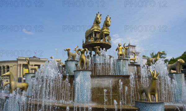 Golden horses and ram statues surrounded by water fountains against an architectural backdrop,