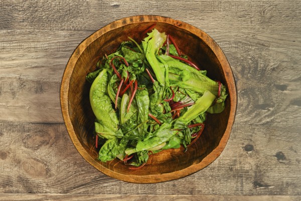 A wooden bowl filled with steamed greens on a rustic wooden tabletop. The leafy vegetables,