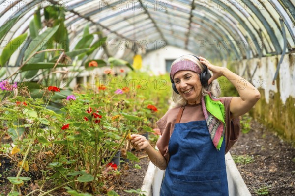 Senior woman smiling, wearing an apron and headphones, happily tending to potted plants and flowers