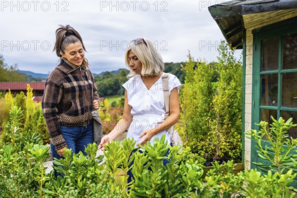 Two women, a mother and daughter, enjoying a shared activity outdoors, carefully selecting plants