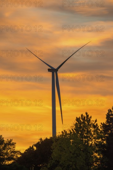 Stationary wind turbine, wind turbine, rotor blades and generator, silhouette, atmospheric sky in