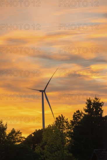 Stationary wind turbine, wind turbine, rotor blades and generator, silhouette, atmospheric sky in
