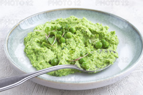 A vibrant green pea puree fills a shallow bowl, topped with fresh peas and microgreens. The dish