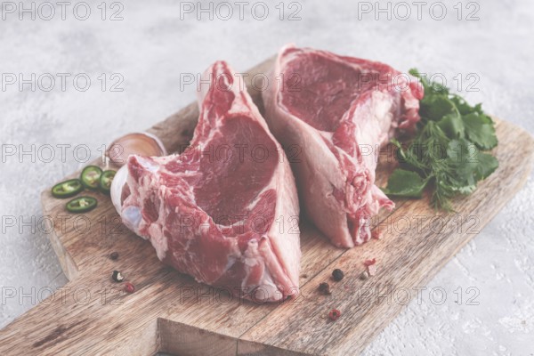 Fresh pieces of beef on the bone, on a wooden cutting board, with herbs and spices, ready for