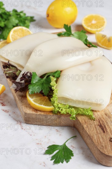 Fresh squid prepared for cooking, surrounded by herbs and lemon, placed on a wooden chopping board