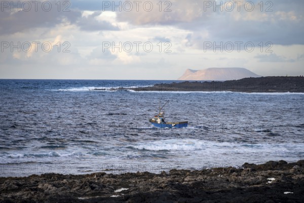 Fishing boat out to sea in the evening, seaside coast with volcanic rocks at sunset, La Santa,