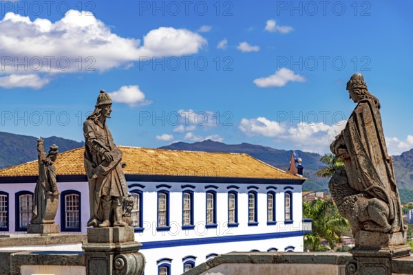 Statues of biblical prophets sculpted by Aleijadinho with ancient buildings and mountains in the